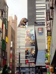 Ein riesiger Godzilla schaut hinter dem Kino hervor.